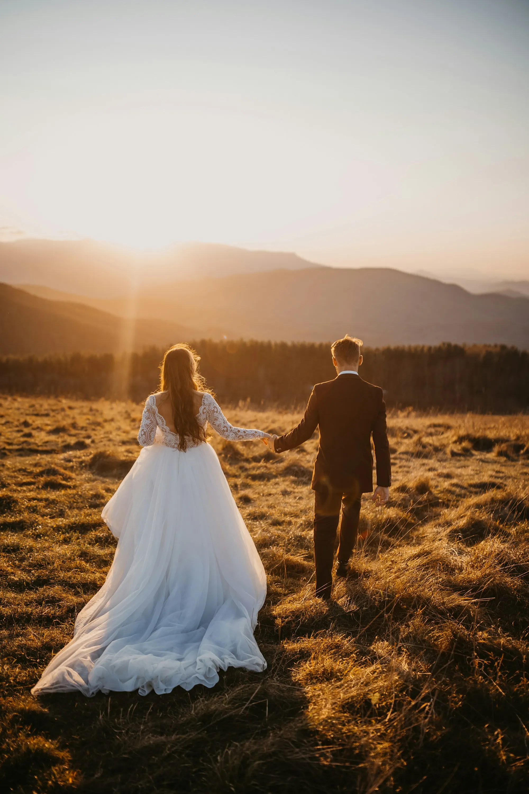 Casal de noivos caminhando num campo ao pôr do sol